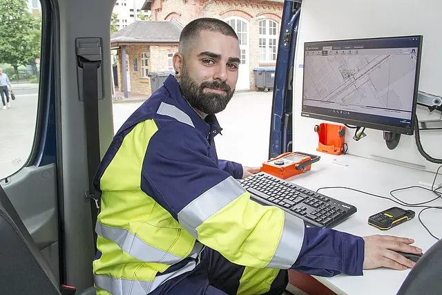 Ein Mitarbeiter des NBB Entstörungsdienstes in seiner Arbeitskleidung sitzt vor einem Bildschirm in einem Fahrzeug. Auf dem Bildschirm ist ein Kartenausschnitt zu sehen.